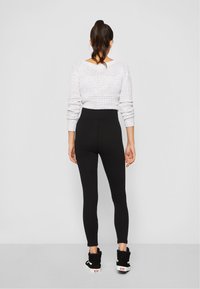 Svarta högmidjade leggings tillsammans med en vit strukturerad stickad tröja med långa ärmar och en öppen ryggdesign. Svarta skor ingår.