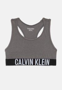 Grå sports-bh laget av mykt stoff, med racerback-design. Svart elastisk band med hvit "CALVIN KLEIN" logo nederst.