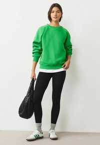 Zaļš džemperis ar ribotām piedurknēm, apvienots ar melniem ribotiem legingiem. Baltas sporta apavi ar zaļām svītrām un teksturēta melna soma.