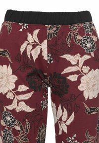 Leggings mit floralem Muster auf maroonfarbenem Hintergrund, die beige und schwarze Blumen zeigen. Elastischer schwarzer Bund, weiche Stofftextur.