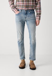 Light blue denim jeans with a slim fit, featuring distressed details and subtle fading. Worn with a plaid shirt and brown loafers.
