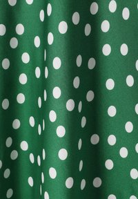 Tissu vert avec une texture lisse, présentant de grands pois blancs uniformément espacés sur la surface.