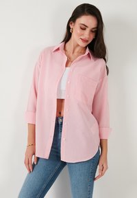 Striped shirt in light pink and white, long sleeves, button-up design, single chest pocket, paired with blue jeans. Textured fabric.