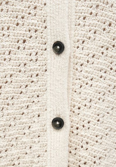 Εκρού πλεκτή ζακέτα με υφητό σχέδιο, κούμπωμα με δύο μαύρα κουμπιά και απαλή, ελαφριά αίσθηση.
