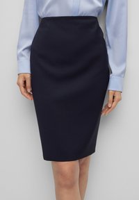 Jupe crayon bleu marine en tissu lisse, présentant une silhouette ajustée qui tombe juste en dessous du genou avec un léger éclat.
