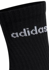 Chaussettes noires côtelées en matériau doux avec le texte blanc "adidas" près de la cheville. Design classique, adapté à un usage quotidien.