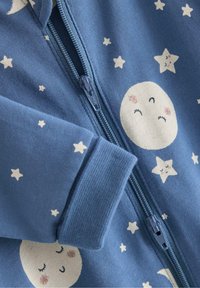 Blauwe onesie met ritssluiting, gemaakt van zachte stof, met witte maan- en sterrenpatronen, voorzien van een gestructureerde boord en een bijpassende ritssluiting.