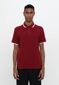 Burgunderfarget polo-skjorte laget av bomull, med krage i klassisk stil, tre-knappe lukking, og hvite striper som aksenter på kragen og ermene.