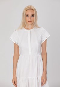 Robe en coton blanc à manches courtes, col rond, boutonnée à l'avant et jupe à volants. Présente une couture décorative le long des bords des manches.