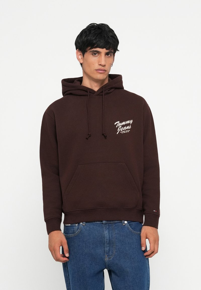 Bruine hoodie van een katoenmix met een voorkantzak, capuchon met trekkoord en een wit "Tommy Jeans" logo aan de linkerkant. Casual fit ontwerp.