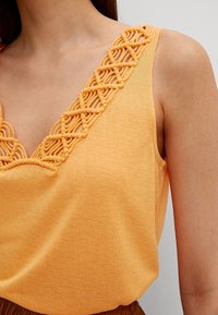 Top arancione senza maniche con un design incrociato testurizzato lungo la scollatura. Tessuto morbido con una vestibilità morbida.