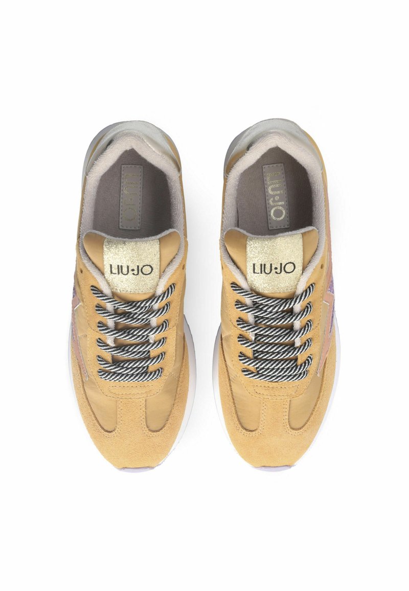 Zapatillas de ante amarillo claro con acentos metálicos, cordones tonales y una suela acolchada. Presenta un logo en la lengüeta y el talón.