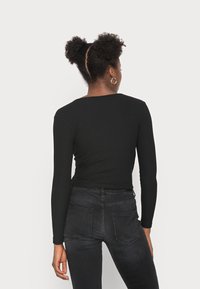 Schwarzes, geripptes Langarmoberteil mit einem Scoop-Back-Design, kombiniert mit dunklen Jeans aus Denim mit Gesäßtaschen und einer taillierten Silhouette.