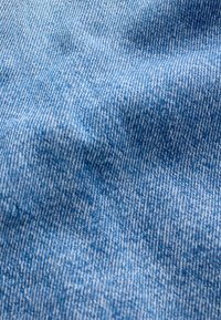 Gros plan d'un tissu denim bleu clair montrant la texture du tissage diagonal et des plis subtils.