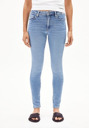 Hellblaue Skinny Jeans aus Denim, mit mittelhoher Taille, zwei Vordertaschen und schmaler Passform, kombiniert mit schwarzen Riemchensandalen.