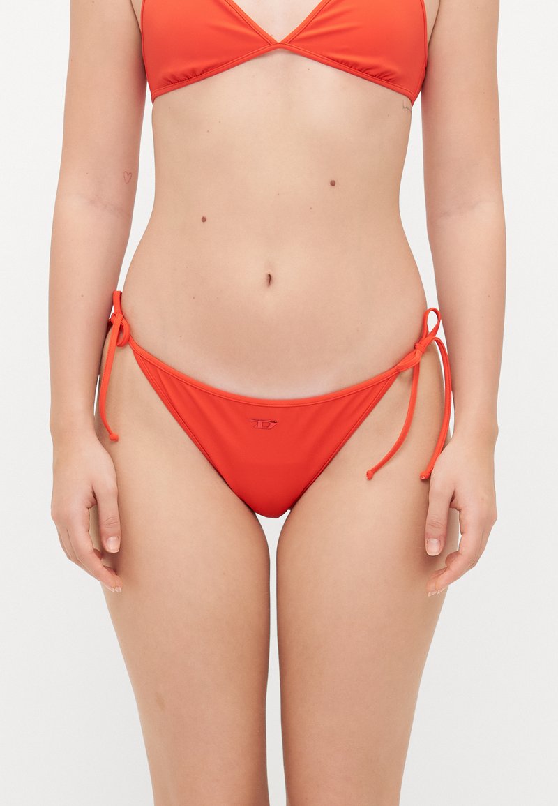 Raudonas bikini komplektas, turintis trikampį viršutinį trikotažą ir reguliuojamas apatinės dalies juostas, pagamintas iš lygaus, elastingo audinio su minimaliu logotipo detaliu.