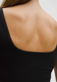 Crna majica bez rukava s širokim izrezom, glatke teksture, i malim logotipom na leđima. Koža vidljiva oko izreza.