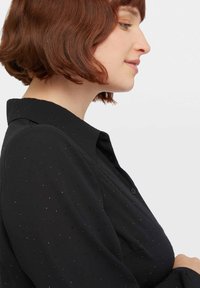 Camicia nera con bottoni, realizzata in un tessuto testurizzato con piccoli dettagli simili a perline lucide. Collo classico e maniche lunghe.