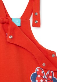 Jumpsuit de algodón rojo para bebé con tirantes ajustables y cierres a presión. En la parte frontal presenta un diseño bordado de un lazo con lunares.