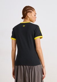 Black t-shirt with yellow accents, short sleeves, and a round neckline. Features a small yellow logo on the upper back. Smooth cotton texture.