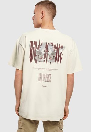 Kræmfarvet t-shirt med et grafisk motiv af to duer, fed skrift og tekst nedenfor. Casual pasform med korte ærmer og blød tekstur.
