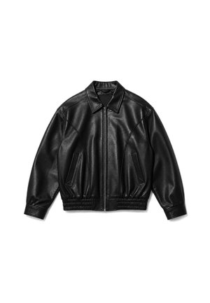 Person wearing a black leather jacket with embossed snake and leaf design and the word "VERTERE" on the back, paired with white pants.