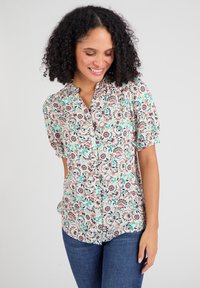 Bloes met bloemenpatroon in lichte stof, voorzien van een knoopsluiting aan de voorkant, korte pofmouwen en een pastel kleurenschema met complexe patronen.