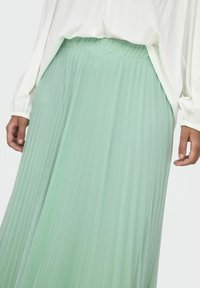 Záhybová sukňa mentolovej zelenej farby vyrobená z ľahkého materiálu s elastickým pásom. Plynulý dizajn siahajúci do polovice lýtok.