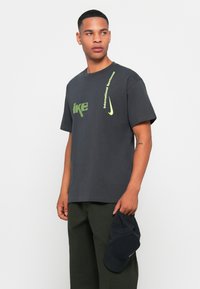 Grå bomulds t-shirt med fremtrædende grøn Nike branding og teksten "International Sportswear". Enkel, afslappet pasform med korte ærmer.