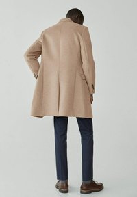 Beige wollen jas met een relaxte fit, voorzien van een rugventilatie, lange mouwen en knoopaccenten op de manchetten, gecombineerd met donkerblauwe maatwerk broek.