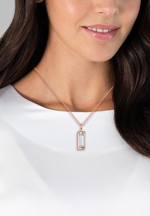 Collier pendentif en or rose avec un cristal rectangulaire facetté sur une fine chaîne. Surface lisse avec une finition brillante, porté sur un haut blanc.