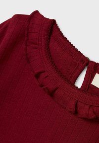 Bordeauxfarbenes, geripptes Oberteil mit einem gerafften Ausschnitt; verfügt über einen Knopfverschluss am Rücken. Weiche Textur und dezente Details.