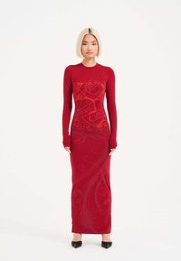 Vestido rojo ajustado con mangas largas, con un patrón floral y texto en escritura. Hecho de una tela elástica, con una silueta larga y estilizada.