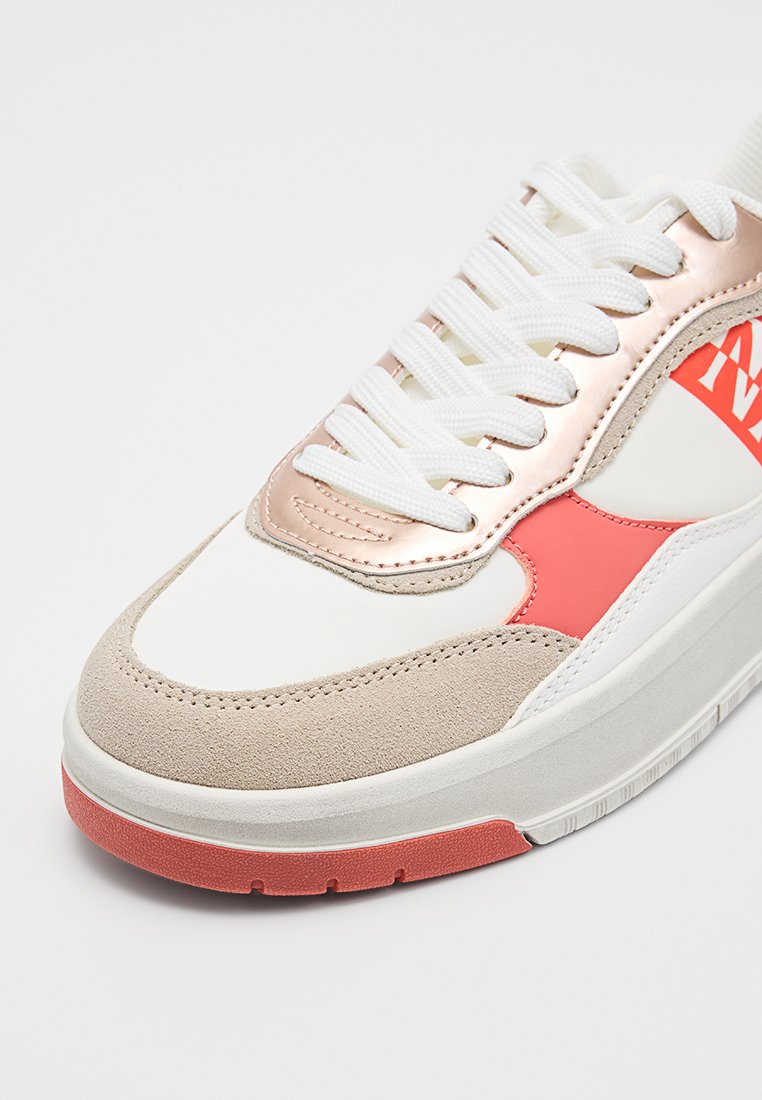 Zapatilla blanca con puntera de ante beige, panel de ojales metálicos en oro rosa, detalles en coral, cordones blancos y suela de goma con detalle en coral.