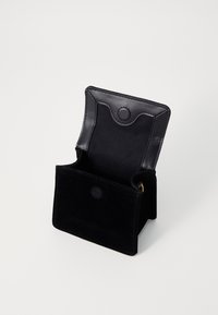 Svart semsket lommebok med lærklaff, med en sirkulær trykknaplukking og et åpent rom for lagring. Glatt tekstur og minimal design.