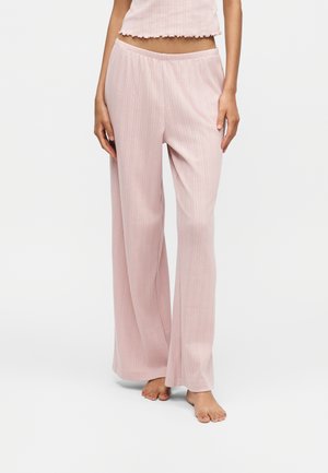 Femme portant un pantalon large côtelé rose clair et un top court assorti, debout pieds nus sur fond blanc.