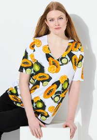 Top de manga corta con escote en V que presenta un colorido estampado de frutas como papayas, naranjas y limones sobre un fondo blanco. Textura de tela suave.