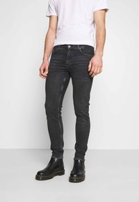 Svarta smala jeans med en subtil bleknad textur. Innehåller framfickor, knappstängning och är ihopparade med svarta ankelboots.