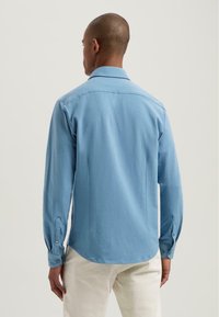 Camicia azzurra chiara realizzata in un tessuto morbido, con colletto, maniche lunghe con polsini abbottonati e un orlo curvo.