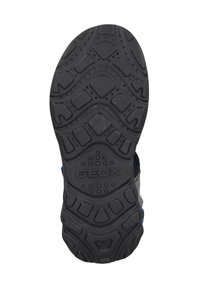 Suela de zapato de goma negra con patrones de agarre texturizados. Presenta un logotipo elevado "GEOX" y orificios de ventilación a lo largo del diseño.