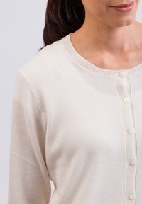 Ljus krämfärgad cardigan i ett mjukt stickat tyg, med rund hals och sex knappstängningar framtill samt en ribbad krage.
