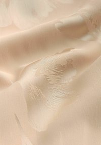 Tissu beige doux avec une texture jacquard florale subtile, délicatement plié pour montrer les détails lisses et en relief du motif tissé.