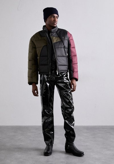 Pamušalas striukė su juoda, žalia ir burgundiška spalvų blokais; blizgūs juodi vinilo keliai; juodi kulkšninių botai; stovi ant pilko grindų.