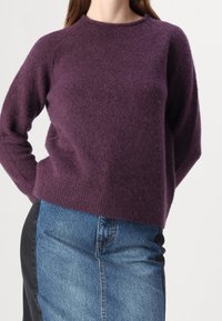 Violetti neulottu pusero pyöreällä pääntiellä ja raglan-hihoilla, yhdistettynä farkkuhameeseen, jossa on mustat sivupaneelit.