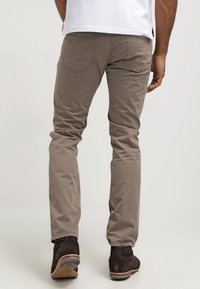 Bruine katoenen broek met rechte pasvorm, twee achterzakken en subtiele stiksels. Draagt met zwarte enkellaarsjes.