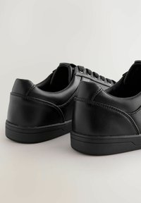 Svarta låga sneakers i slät syntetisk material, med rund tå, snörning framtill och texturerade detaljer på sidorna.