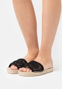 Černé háčkované pantofle s tkaninou na svršku a přírodní juteovou podrážkou. Disponují otevřenou špičkou a texturovanými detaily.