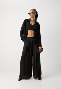 Black outfit featuring a cropped top, button-up shirt, and wide-leg pants. Smooth, lightweight fabric with a sleek, modern design. Sunglasses and clutch bag included.