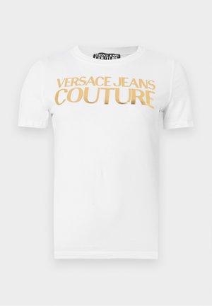 Bílá tričko s krátkými rukávy a zlatým nápisem "VERSACE JEANS COUTURE" potisknutým přes hrudník.