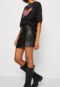 Camiseta gráfica negra con un diseño colorido de mariposa, combinada con una falda mini de cuero sintético negra con una abertura frontal y botas negras hasta la rodilla.